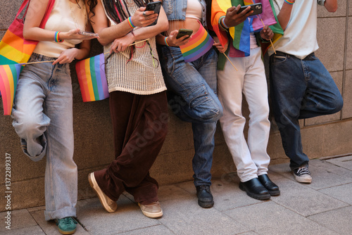Obraz na płótnie Young people using smartphones and holding rainbow flags are leaning against a wall w salonie