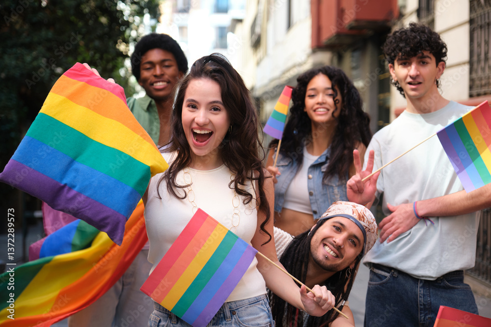 Happy multi ethnic friends having fun together during LGBT pride parade, waving rainbow flags and smiling