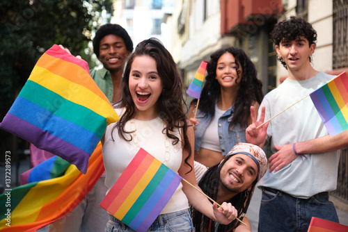 Happy multi ethnic friends having fun together during LGBT pride parade, waving rainbow flags and smiling