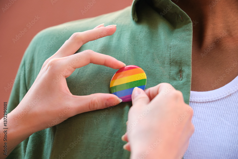 Hands pinning rainbow badge on green shirt, lgbtq plus concept