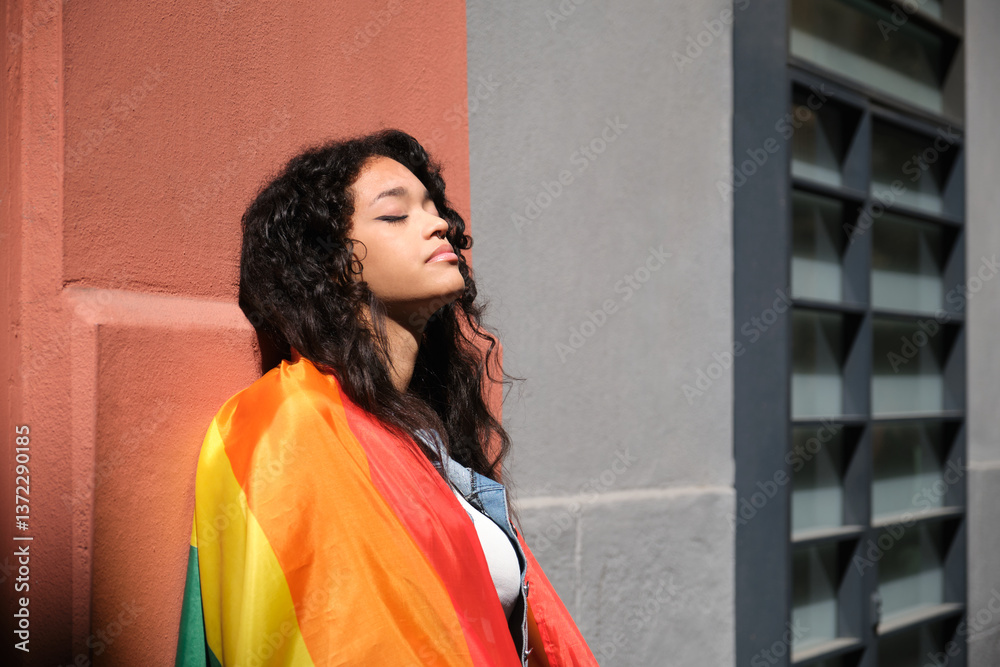 Young woman with closed eyes holding rainbow flag, celebrating LGBT pride and feeling sense of belonging