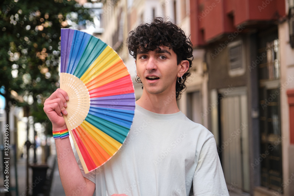 Young man holding rainbow hand fan celebrating LGBT pride in the city