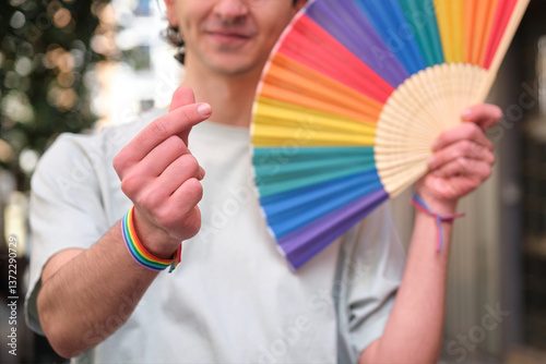 Obraz na płótnie Young man making Korean finger heart and showing rainbow fan celebrating LGBT pride w salonie