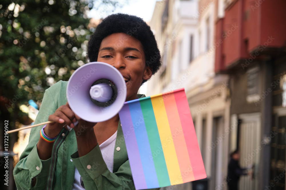 Young man holding rainbow flag and using megaphone promoting equal rights and freedom at lgbt pride parade