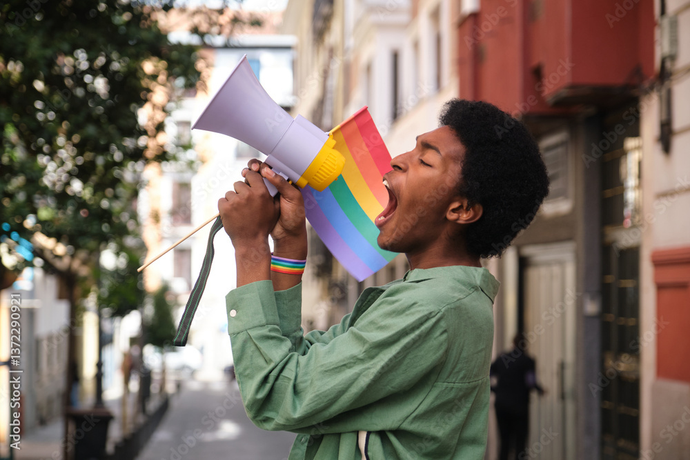 Young man holding rainbow flag and screaming on megaphone at a LGBT pride parade