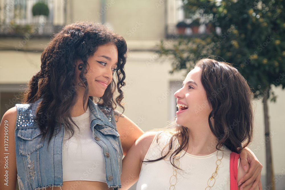 Two happy female friends are walking arm in arm on a city street, enjoying each other's company and sharing a laugh