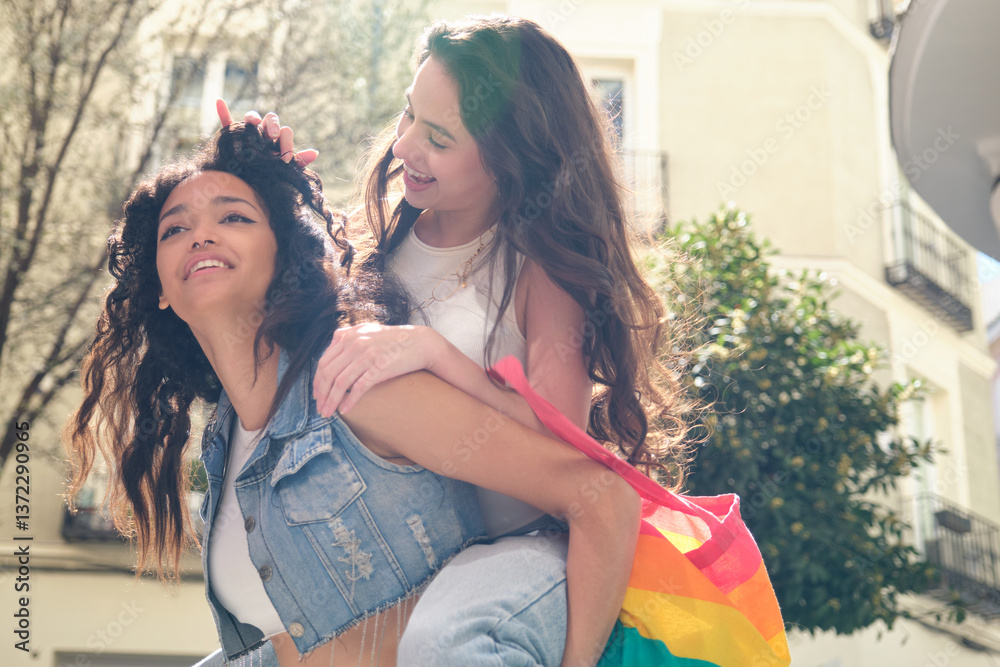 Two smiling women playing together in the city with rainbow tote bag