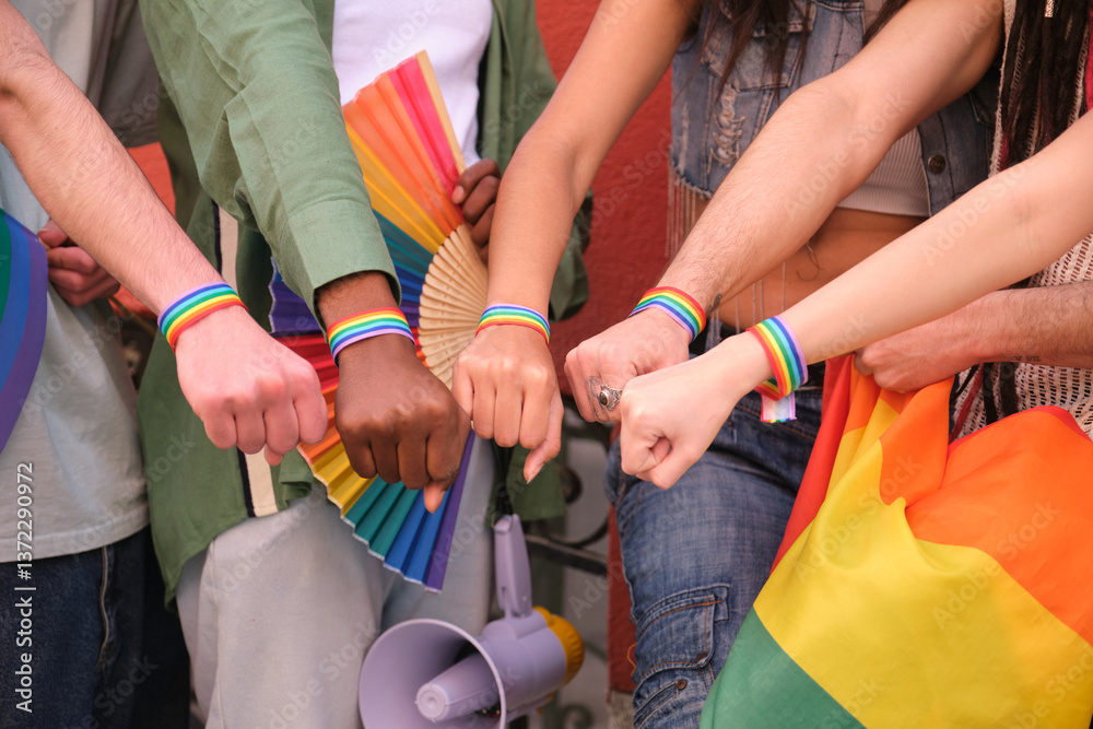 Activists wearing rainbow bracelets and holding rainbow flags and fans showing their fists at a LGBT pride parade