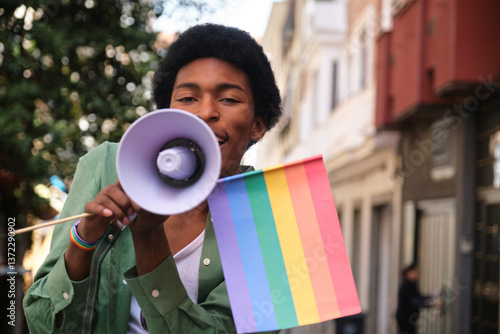 Obraz na płótnie Young man holding rainbow flag and using megaphone promoting equal rights and freedom at lgbt pride parade w salonie
