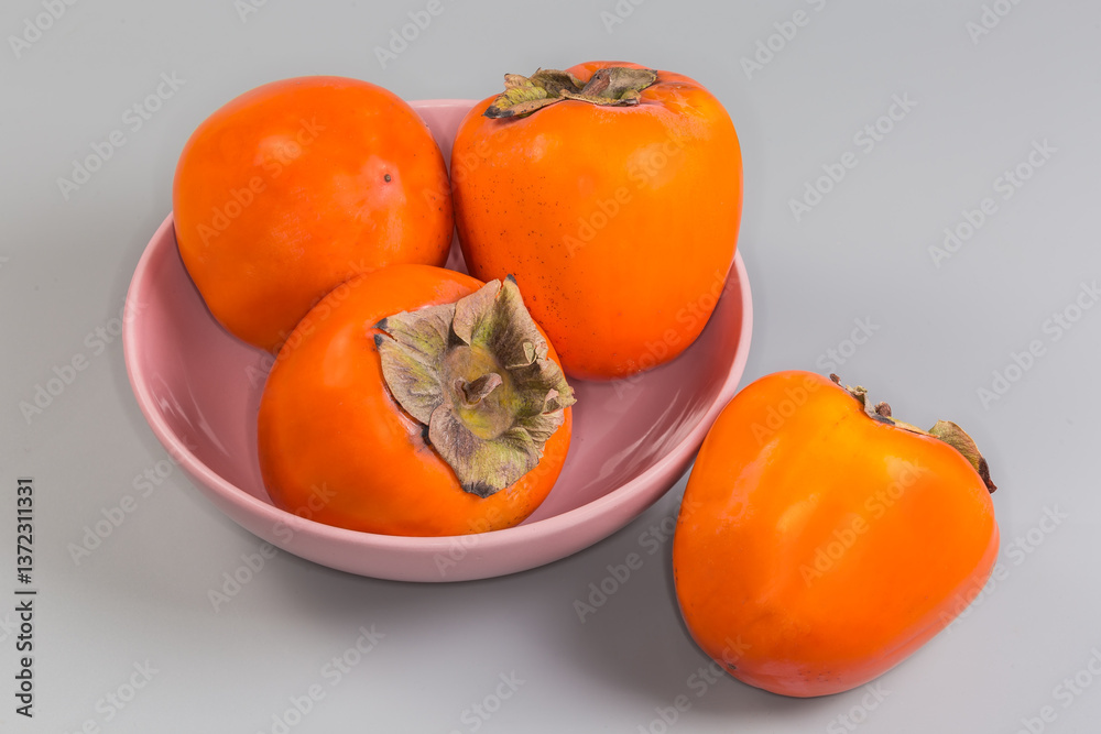Εκτύπωση καμβά Persimmon fruits in pink bowl and beside on gray background