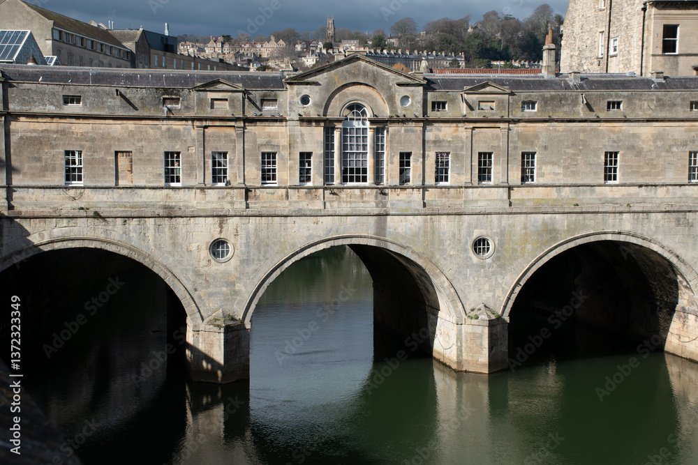 Obraz premium Pulteney Bridge in Bath, England, showcasing its historic architecture over the serene river. A beautiful landmark surrounded by nature and city life.