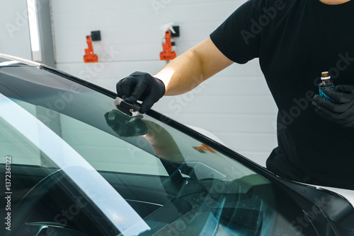 A master in black gloves applies a nano protective coating to a car windshield.