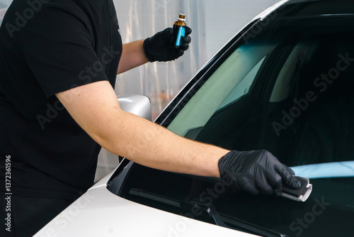 A master in black gloves applies a nano protective coating to a car windshield.