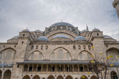 Majestic view of the Süleymaniye Mosque in Istanbul showcasing its grand Ottoman architecture, cascading domes, intricate stonework, and serene atmosphere under a cloudy sky with a hint of gold leaves