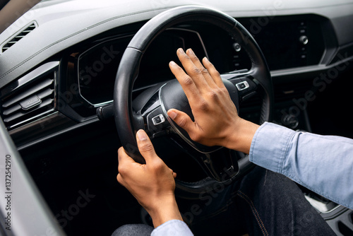 Young black man honking while driving, sitting in car, holding steering wheel, beeping the horn in auto photo