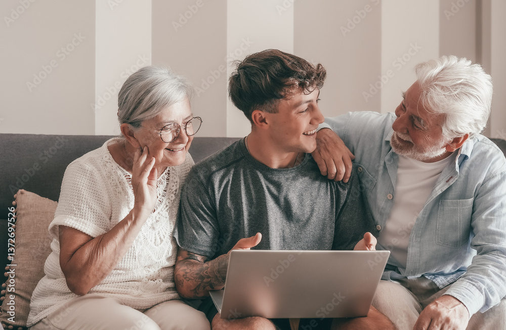 Cheerful Multi generation family of grandparents and young grandson share social media on laptop sitting together on sofa at home. Old couple learning use of computer and technology