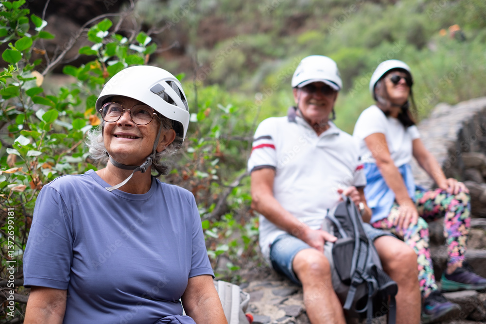 Happy group of seniors hikers with protective helmets resting during an outdoors excursion in mountain, elderly man and women loving freedom and nature and healthy lifestyle