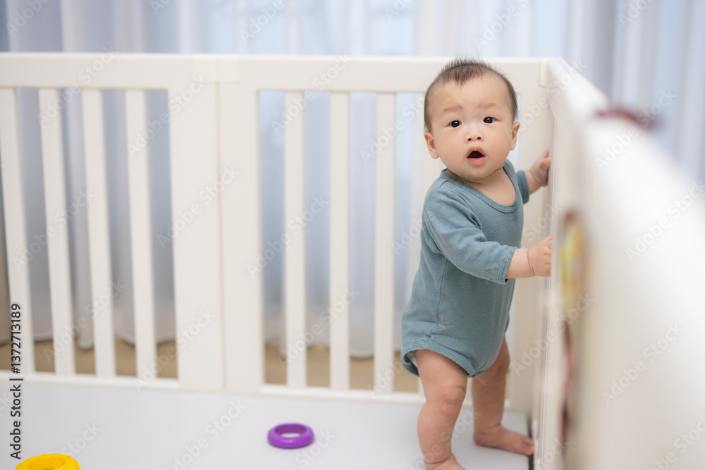Baby standing inside crib holding railing and looking up
