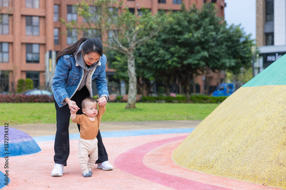 Mother helping baby learn to walk outside