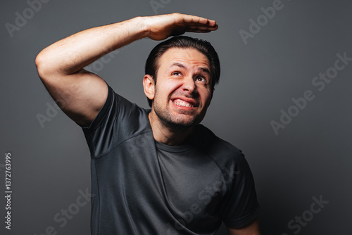 Man covers his head with hand, protecting it from above, emotional portrait on gray background