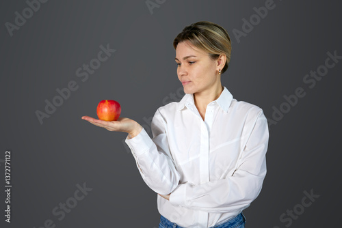 Beautiful blonde woman in white shirt holding red apple in palm. Conceptual photography, teacher, copy space, apple in the palm of your hand, gain new knowledge
