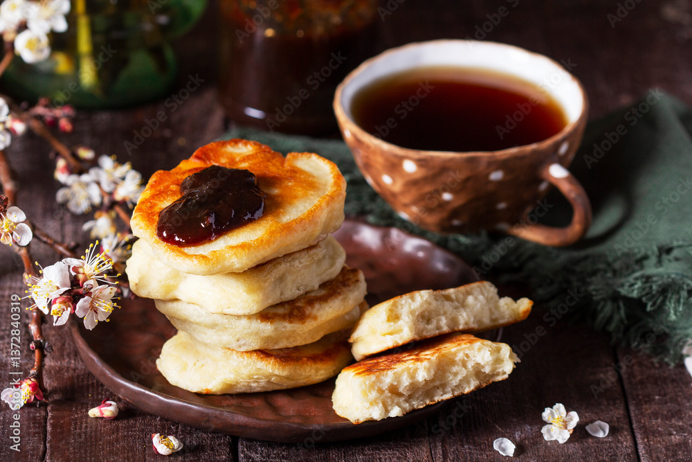 Lenten yeast pancakes with plum jam and tea, and a bouquet of blooming apricot branches on a wooden table.