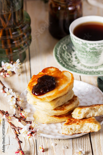 Lenten yeast pancakes with plum jam and tea, and a bouquet of flowering apricot branches on a light wooden table.