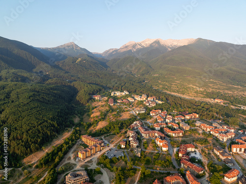 Sunset over Bansko, Bulgaria, with golden light illuminating rooftops and surrounding mountains. Aerial view captures warm evening glow, peaceful atmosphere, and breathtaking natural scenery. Travel