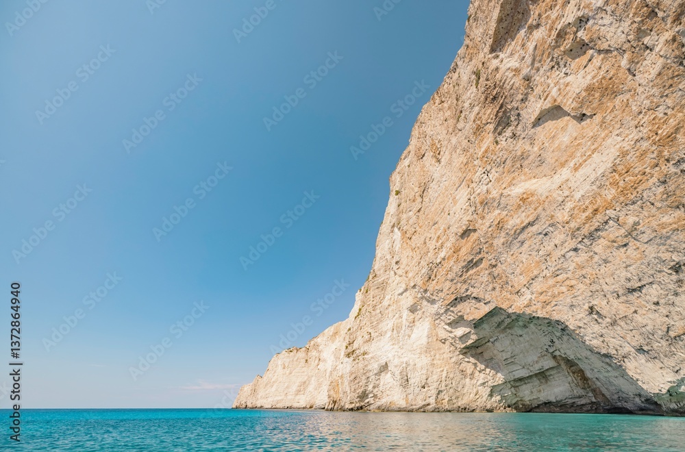 Fototapeta premium Bright sun illuminates towering cliffs above serene blue waters, showcasing the natural beauty of Greece in a peaceful summer landscape ideal for relaxation and exploration