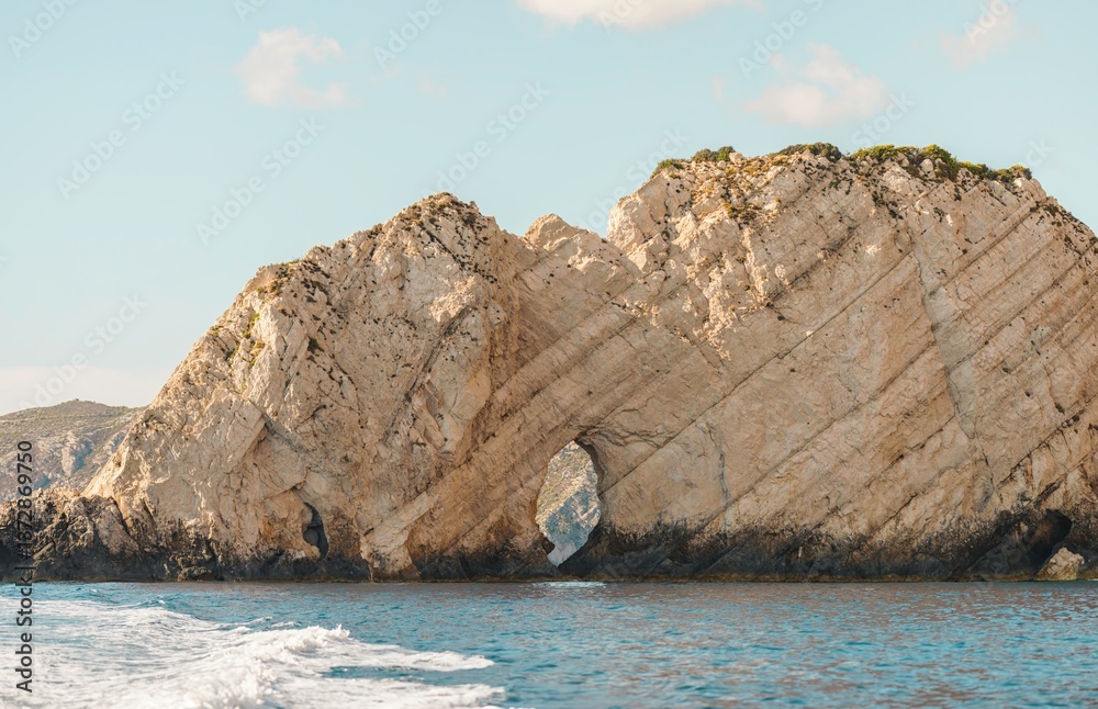 Naklejka premium Guests enjoy a boat trip in Greece, marveling at unique rock formations and natural arches along the coastline under a clear blue sky during summer, creating a perfect getaway experience