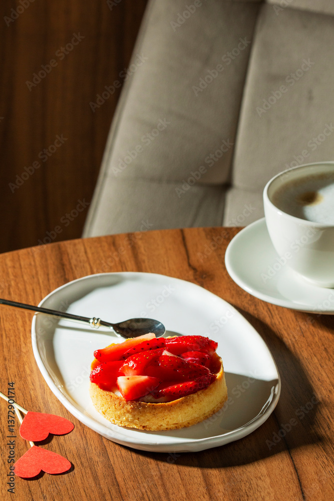 Shortbread cake with custard and strawberries and a cup of latte on a table in a cafe.