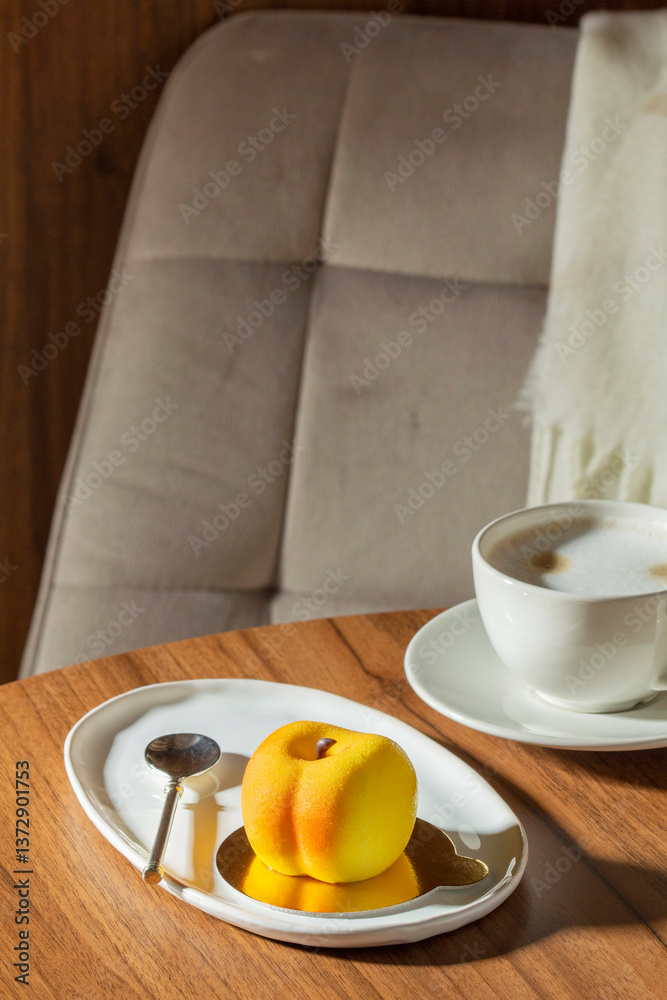 Mousse cake with peach filling covered with velvet glaze and a cup of latte on a table in a cafe.