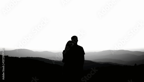 Couple embraces during sunset on a mountain peak, capturing a moment of love and tranquility in nature's beauty