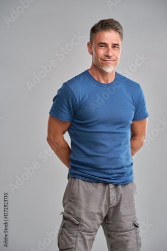 Portrait of confident mature man in casual standing on gray background. Happy older middle aged guy smiling. Healthy active, fit mid adult male in 50s.