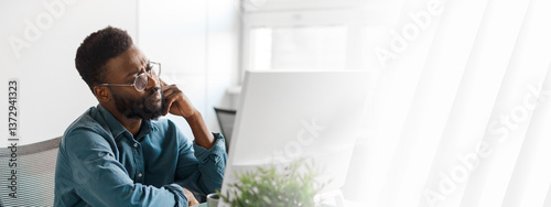 Canvas Print A young African American entrepreneur sits at his desk in a bright office, deep in thought as he focuses on his computer