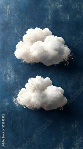 Two fluffy white clouds float against a textured deep blue sky creating a tranquil and dreamlike atmosphere