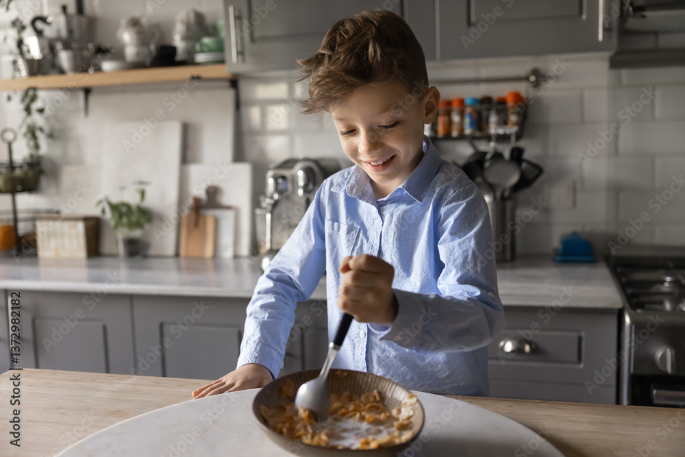 Cute school-age boy standing in domestic kitchen, holding spoon, stirring cereal in bowl, engaged in preparing his breakfast with joyful expression. Balanced food, independence and routine in morning Cute school-age boy standing in domestic kitchen, holding spoon, stirring cereal in bowl, engaged in preparing his breakfast with joyful expression. Balanced food, independence and routine in morning