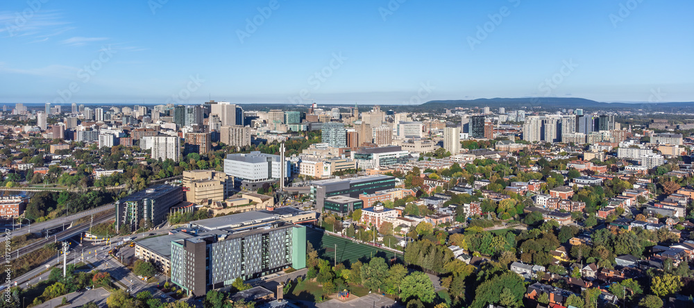Fototapeta premium Aerial panoramic view of downtown Ottawa, including University of Ottawa campus, Sandy Hill, Parliament Hill and Peace Tower, Gatineau Park hills in the backdrop, Ontario, Canada (September 2024)