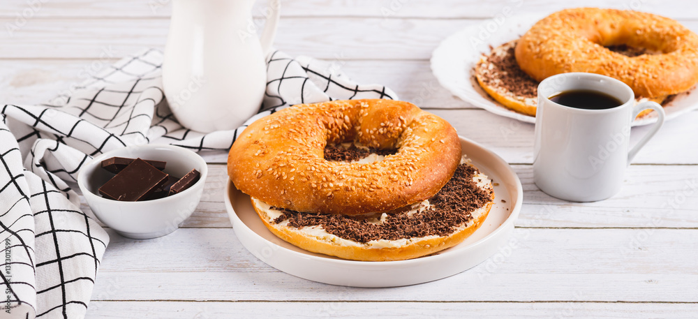 Bagel sandwich with butter and grated chocolate on a plate on a table web banner