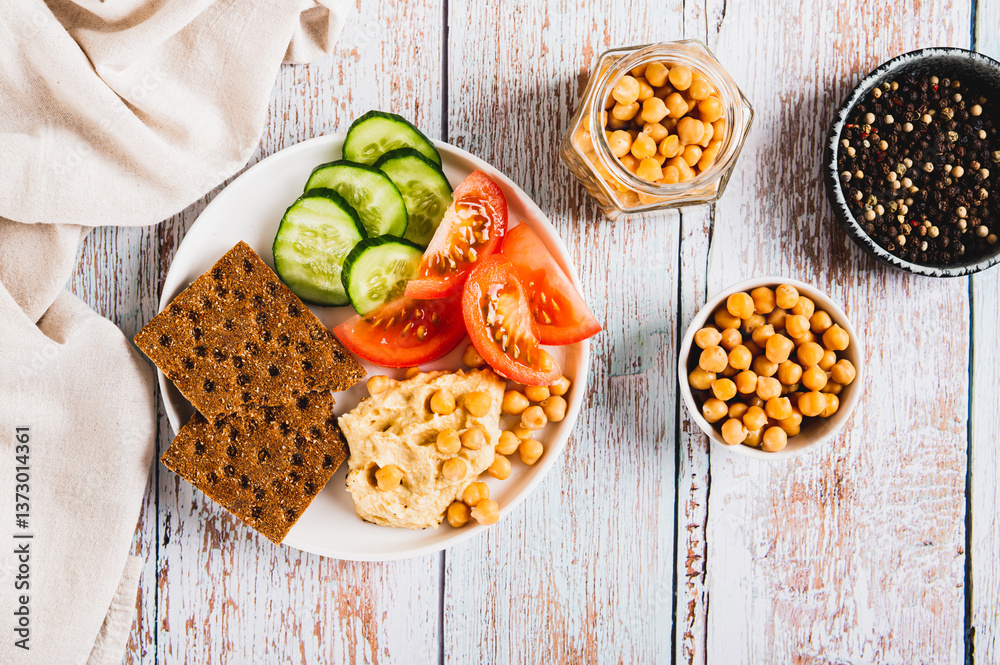 Hummus, chickpeas, tomato, cucumber, grain crackers on a plate on the table top view