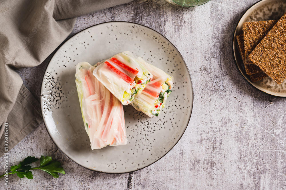 Spring rolls in rice paper with crab sticks, cucumber, greens and sauce on a plate on top view
