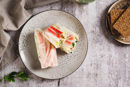 Obraz na płótnie Spring rolls in rice paper with crab sticks, cucumber, greens and sauce on a plate on top view w salonie