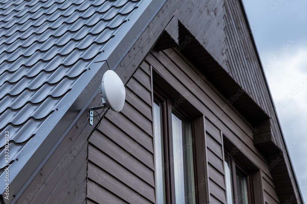 Side view of a modern house with wooden siding, sloped metal roof, large dark framed windows, and a white Wi Fi router mounted near the roofline.