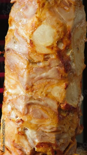 A large Doner kebab rotating in a local restaurant. A pair of rotating skewered chicken and lamb meat grilled and ready to serve in a typical Middle Eastern sandwich	