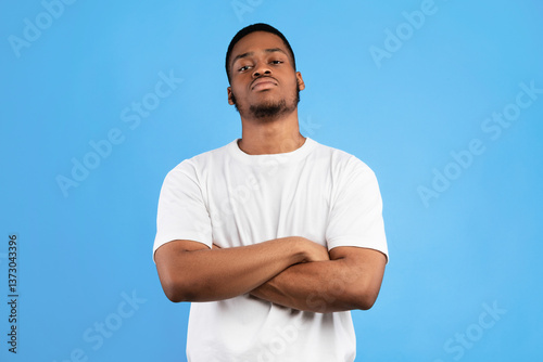 Cool Black Man Standing Crossing Hands Looking At Camera Posing On Blue Studio Background. Menacing Tough Guy's Portrait