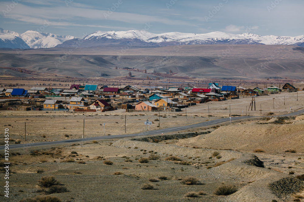 A village with small houses in the Altai Republic, framed by snowy mountains in the background.