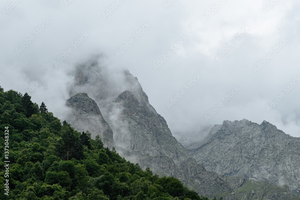 Majestic peaks rise into the cloudy sky, enveloped in mist, while lush greenery flourishes at their base, portraying the serene beauty of northern Ossetia Majestic peaks rise into the cloudy sky, enveloped in mist, while lush greenery flourishes at their base, portraying the serene beauty of northern Ossetia