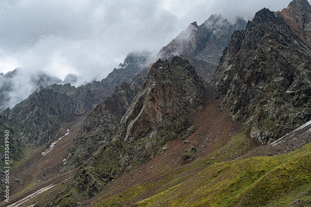 Fototapeta premium In the rugged wilderness of Northern Ossetia, steep mountains rise dramatically against a moody sky. Clouds hover above the peaks, hinting at the beauty of untamed nature waiting to be explored