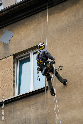 Worker using rope access equipment and safety gear abseils near window on building exterior. Professional maintenance or inspection at height concept