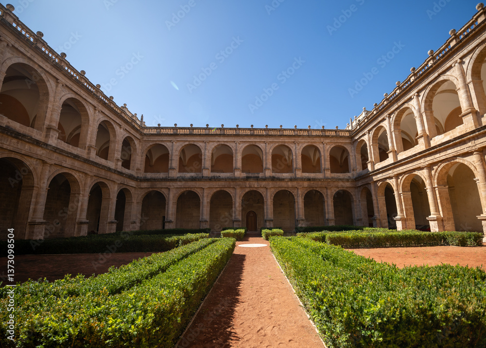 Fototapeta premium Renaissance-style courtyard featuring two-story limestone arcades surrounding formal gardens with geometric hedges under bright Mediterranean sunlight in Valencia, Spain